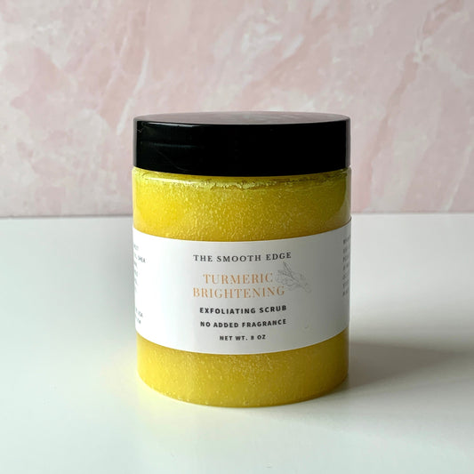 A clear jar with a black lid set on a table with yellow turmeric sugar exfoliating scrub inside. 