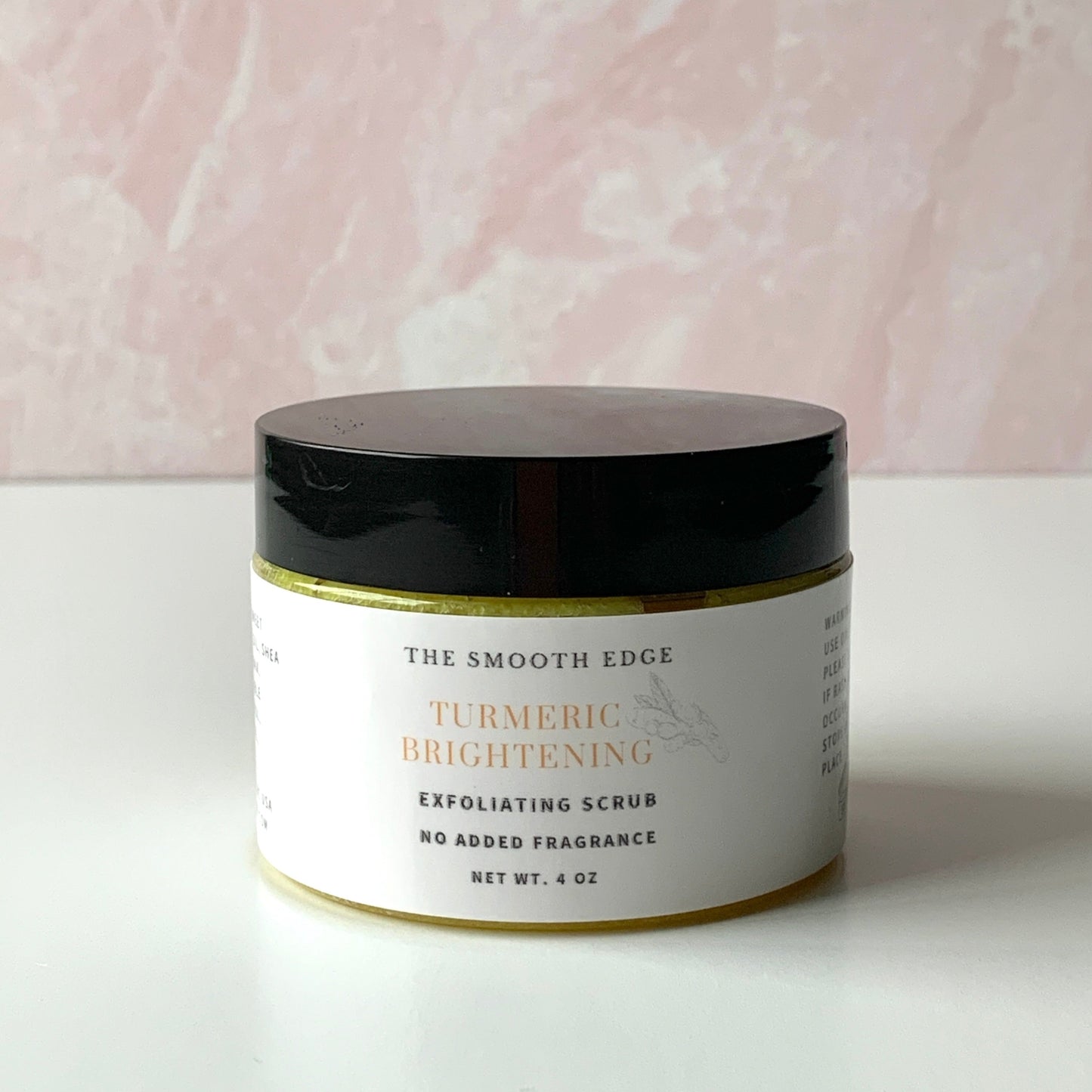 A clear jar with a black lid set on a table with yellow turmeric sugar exfoliating scrub inside.